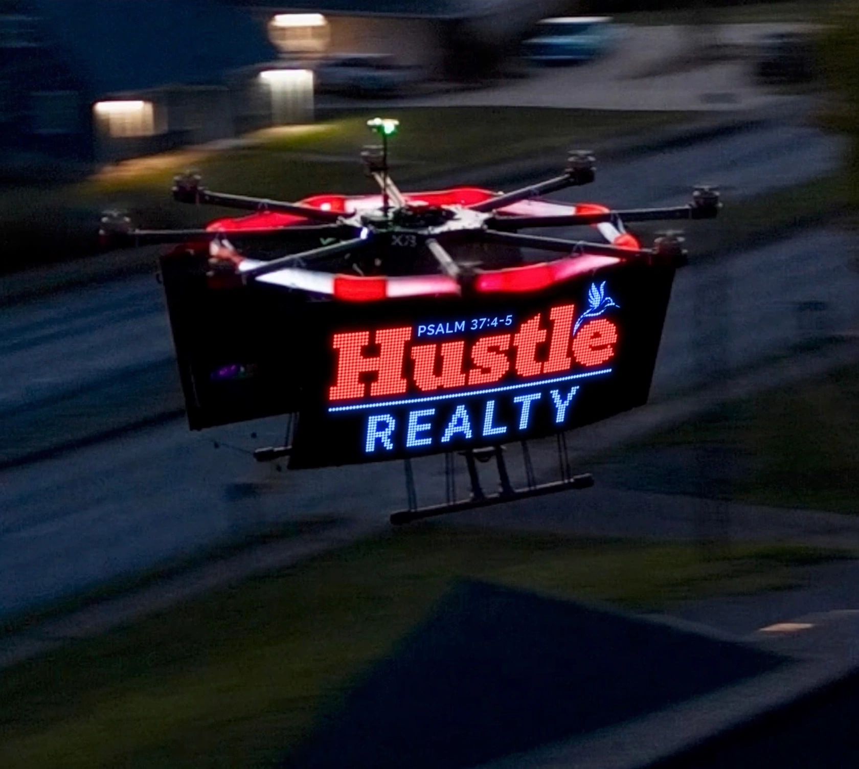 Aerial GraphX drone in flight with a bright Hustle Realty LED advertising display